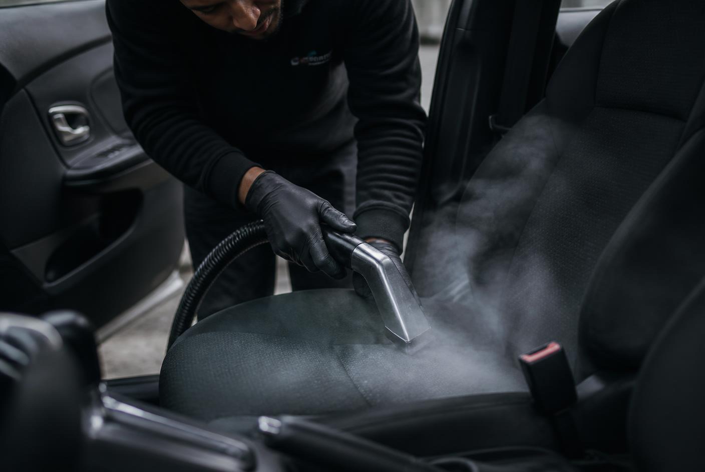 Detailer steam cleaning a car seat during a mobile interior detail in Austin, TX